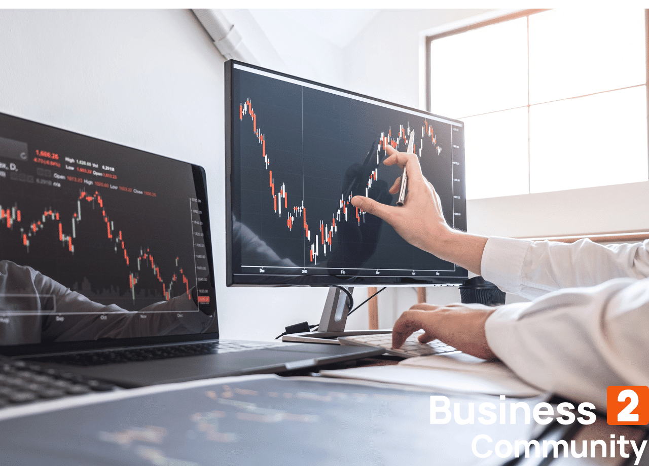 Spot trading grafer vises på to dataskjermer med en hånd som demonstrerer