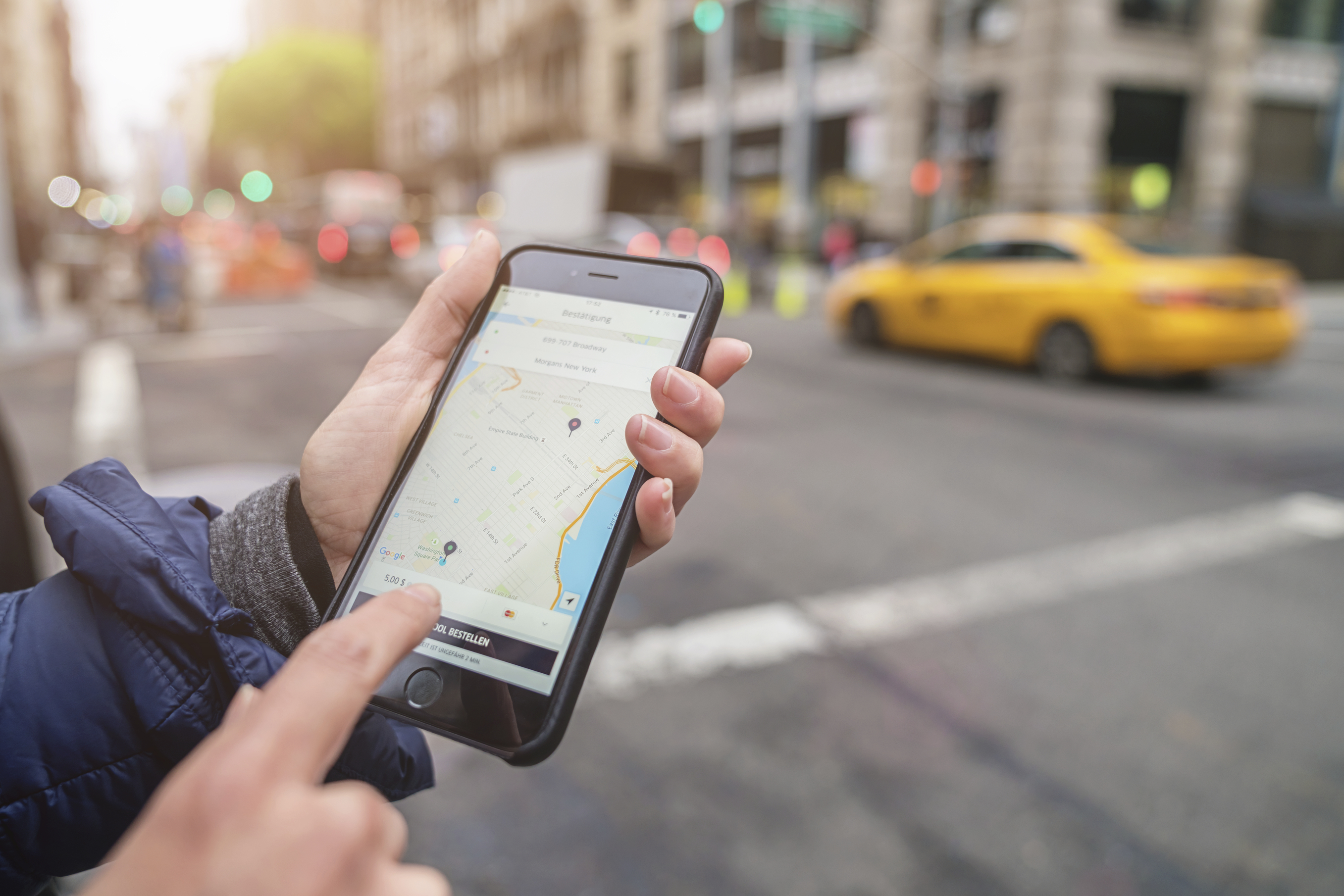 New York, USA - May 6, 2016: Person using the Uber Taxi Cab App on Apple iPhone 6s Plus in the streets of New York City. The classic NYC Yellow Cab, which is the Uber Service Competition unsharp in the background. Uber Inc., based in San Francisco, develops, markets and operates the Uber mobile app, which allows consumers with smartphones to submit a trip request which is then routed to Uber drivers who use their own carr as an alternative to the classic taxi service.